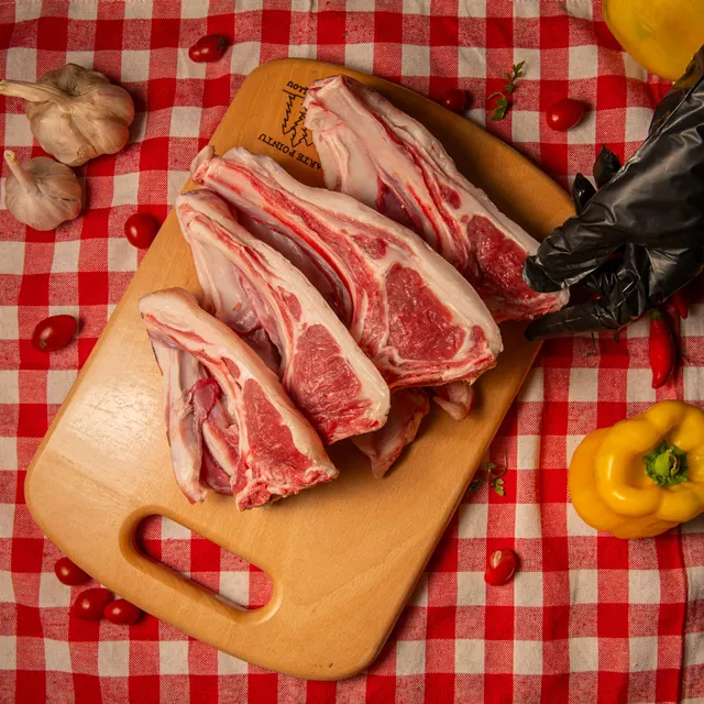 Raw beef ribs on a wooden board over a red checked tablecloth
