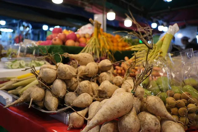 Root vegetables, corn and fruit piled on a farmers' market stall