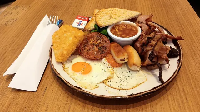 Breakfast plate with sunny-side-up eggs, bacon, baked beans, hash brown and toast