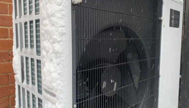 Unité extérieure d'une thermopompe couverte de givre, pendant une chute de neige