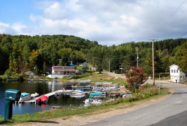 Dock and boats on Lac Papineau in the hamlet of Vernet, with houses and a wooded hill