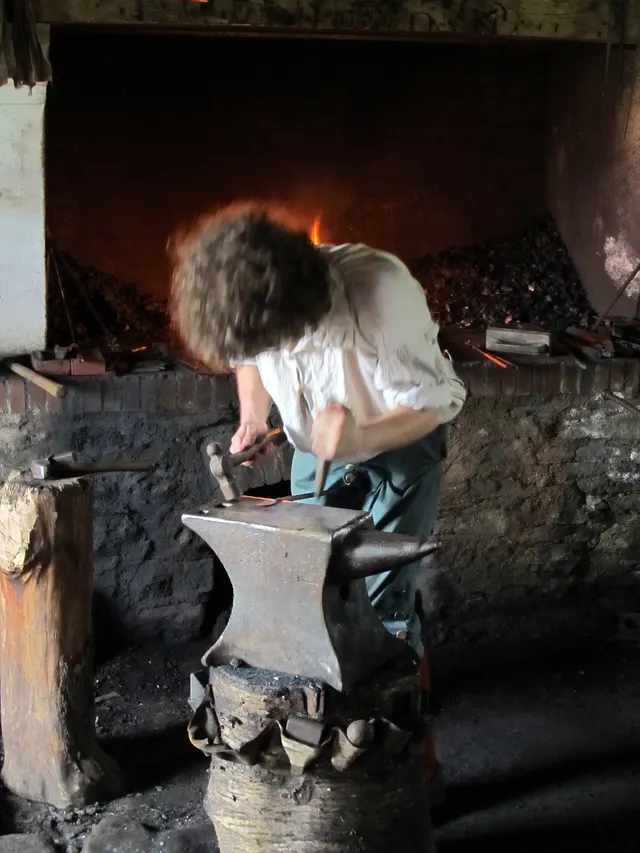 Blacksmith hammering a piece on the anvil in front of the forge