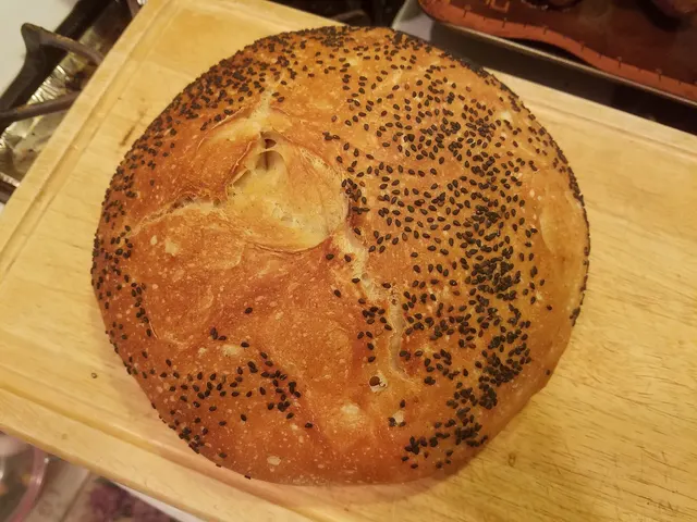 Round sourdough loaf topped with poppy seeds on a wooden board