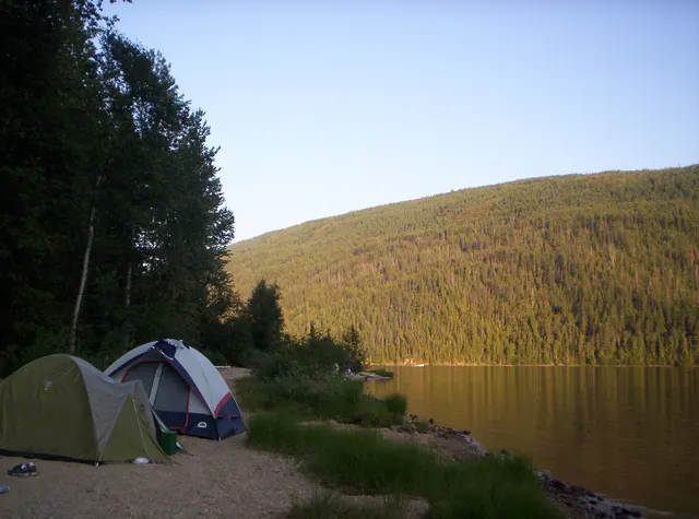 Tents on the shore of Barriere Lake below wooded hills in British Columbia