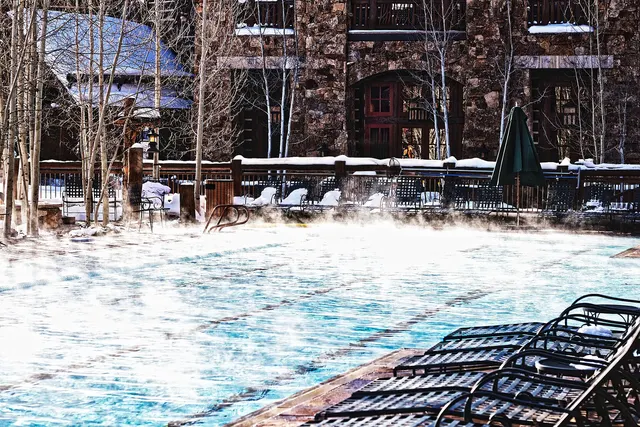 Piscine extérieure chauffée qui fume sous la neige, devant un bâtiment de bois