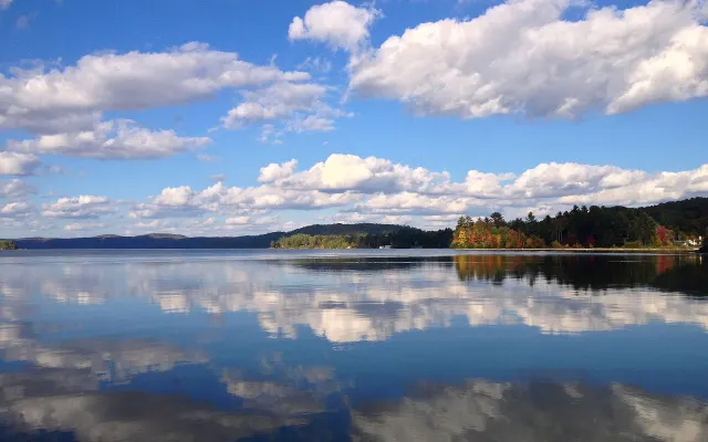 White clouds reflected in Lac Simon, shoreline in fall colours