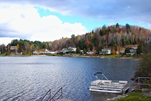 Pontoon boat moored in front of a Lac Simon shoreline lined with houses and fall trees
