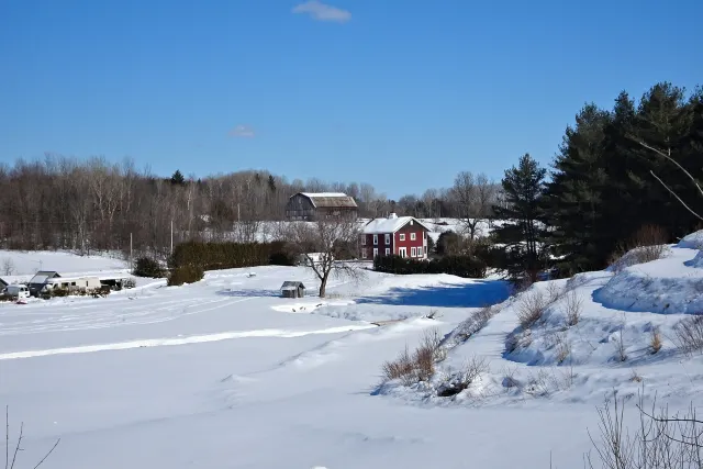 Snowy fields, red farmhouse and barn under a blue sky in Lochaber-Partie-Ouest