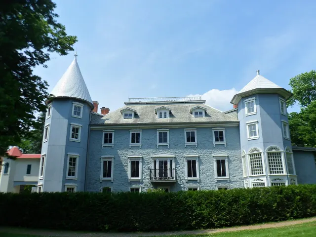 Blue-grey façade of the Papineau manor between its two towers, behind a hedge