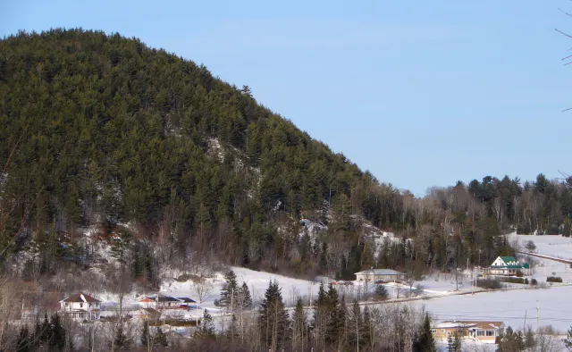 Wooded hill above the houses of Notre-Dame-de-la-Salette, snowy fields