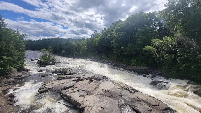 Rapids of the Chutes du Moulin over wide rock slabs under a cloudy sky