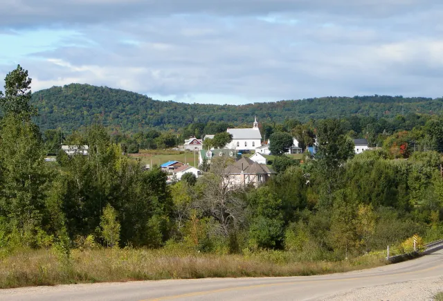 The village of Saint-Sixte and its white church at the foot of wooded hills